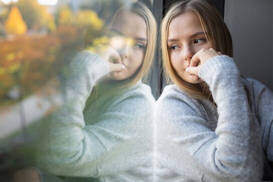 Junge Frau blickt gedankenverloren aus dem Fenster